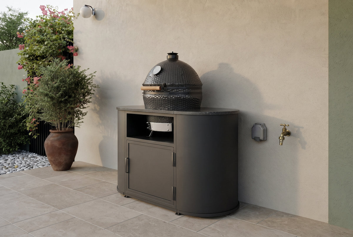 Compacte zwarte buitenkeuken met kamado tegen een tuinmuur, met buitenkraan en stopcontact